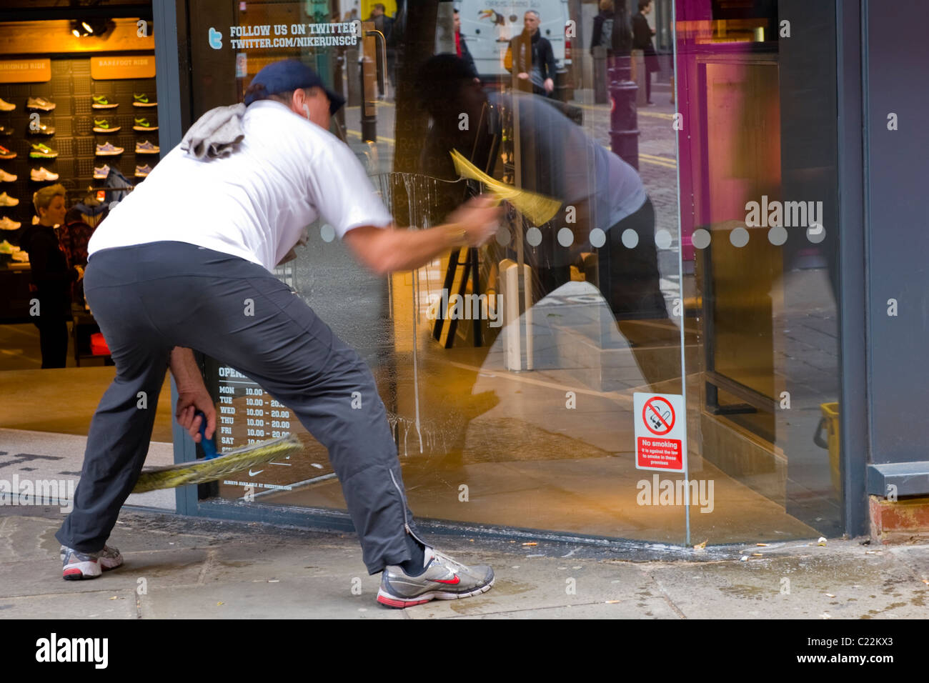 Il Covent Garden , uomo di mezza età in berretto da baseball pulisce negozio o supermercato finestra con spugna e spatola sfocatura del movimento Foto Stock