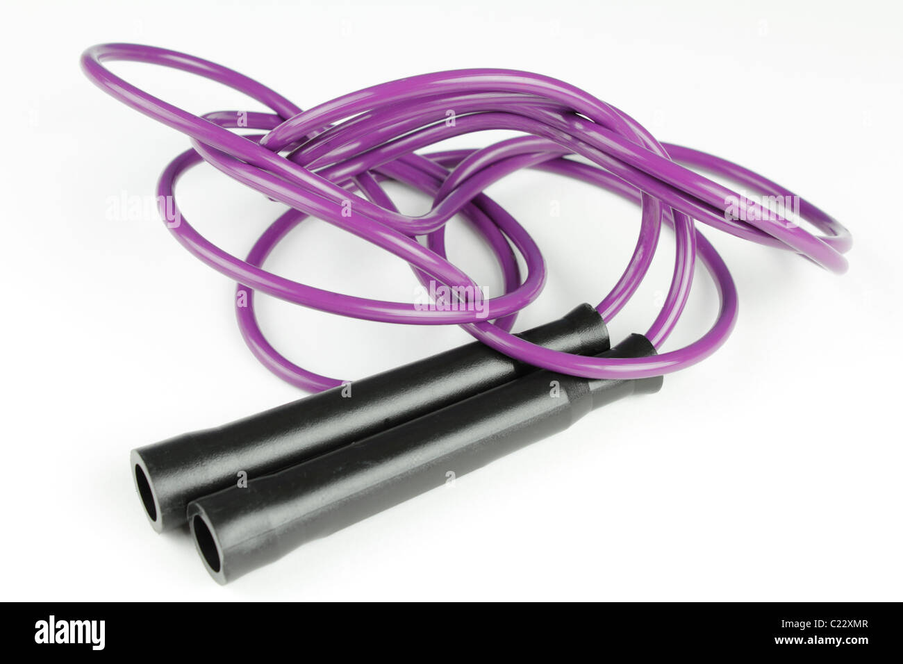 Nero manici in plastica su ciascun lato del viola salto con la corda su uno sfondo bianco. Viola in plastica salto con la corda con maniglie nere su una superficie bianca di close-up Foto Stock