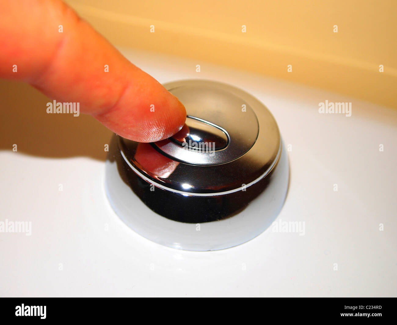 Premere un pulsante su una superficie metallica lucida con un dito in un ambiente pulito e bianco Foto Stock