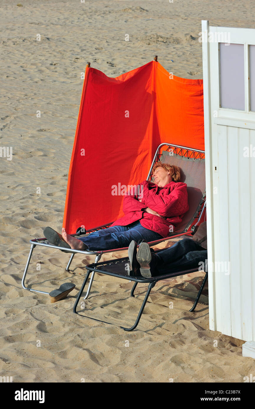 I turisti a prendere il sole alle spalle di frangivento sulla spiaggia durante la primavera, Ostenda, Belgio Foto Stock