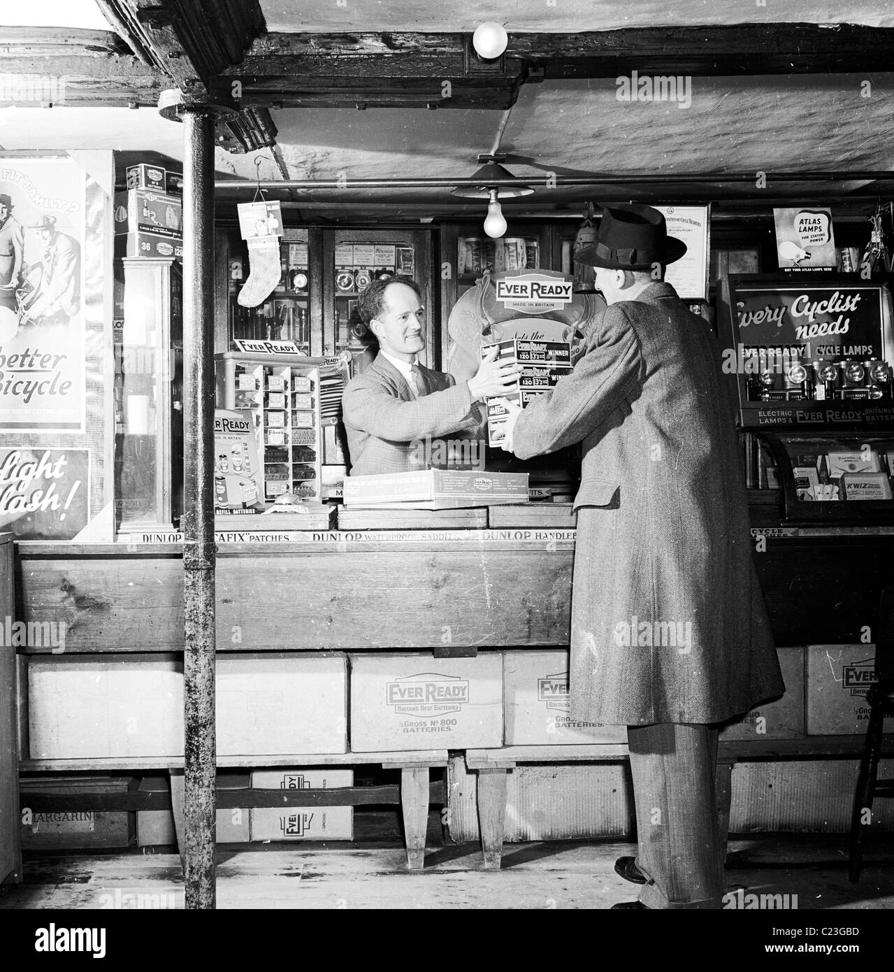 Degli anni Cinquanta, Inghilterra. Venditore per il sempre pronto Battery Company fornisce merci a un negozio di biciclette cliente. Foto Stock