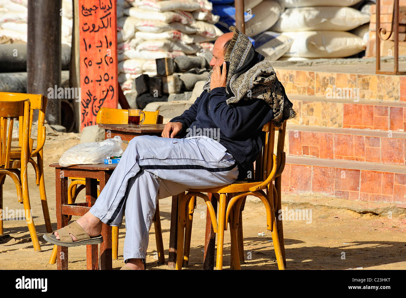 Egyptian uomo seduto su una sedia nella parte anteriore del negozio di caffè e utilizzando un telefono cellulare nella città di Siwa, Western Desert, Egitto Foto Stock