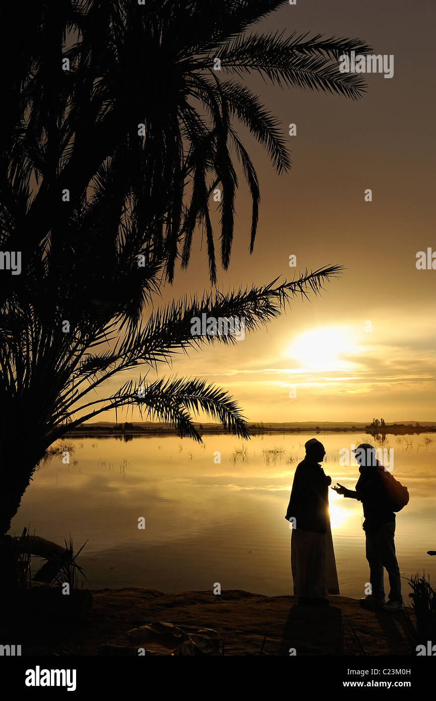 Due egiziani parlando durante un tramonto su un lago salato in Fatnas isola vicino alla città di Siwa, Western Desert, Egitto Foto Stock