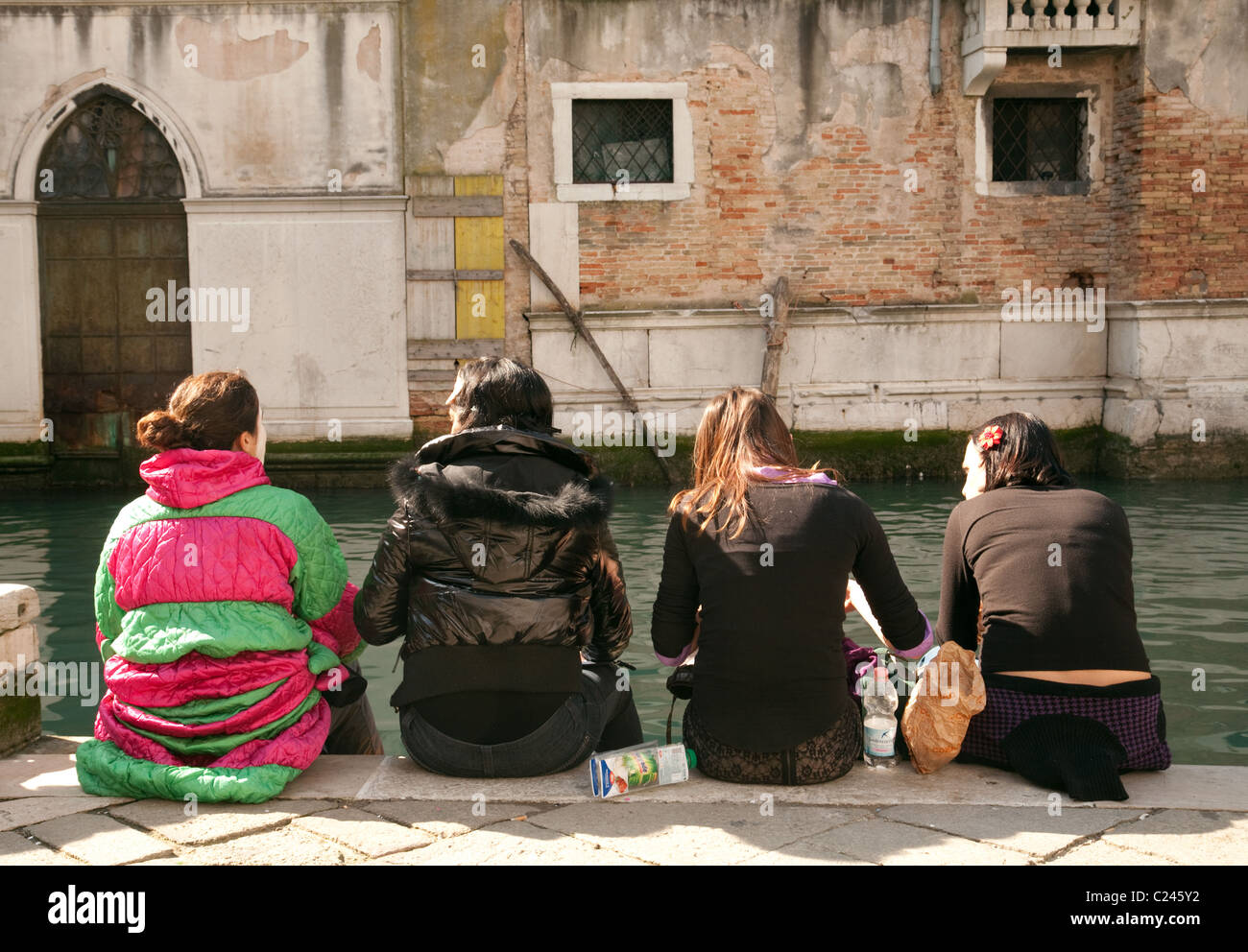 Quattro donne seduti al fianco di un canale dal retro, Venezia Italia Foto Stock