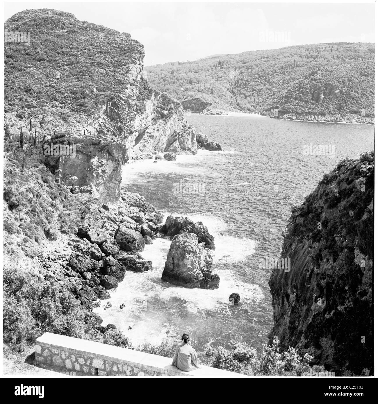 Degli anni Cinquanta, Grecia. Signora seduta sul ponte ammirando il paesaggio della costa dell'isola di Corfù, vicino Palcokstritsa. Foto Stock