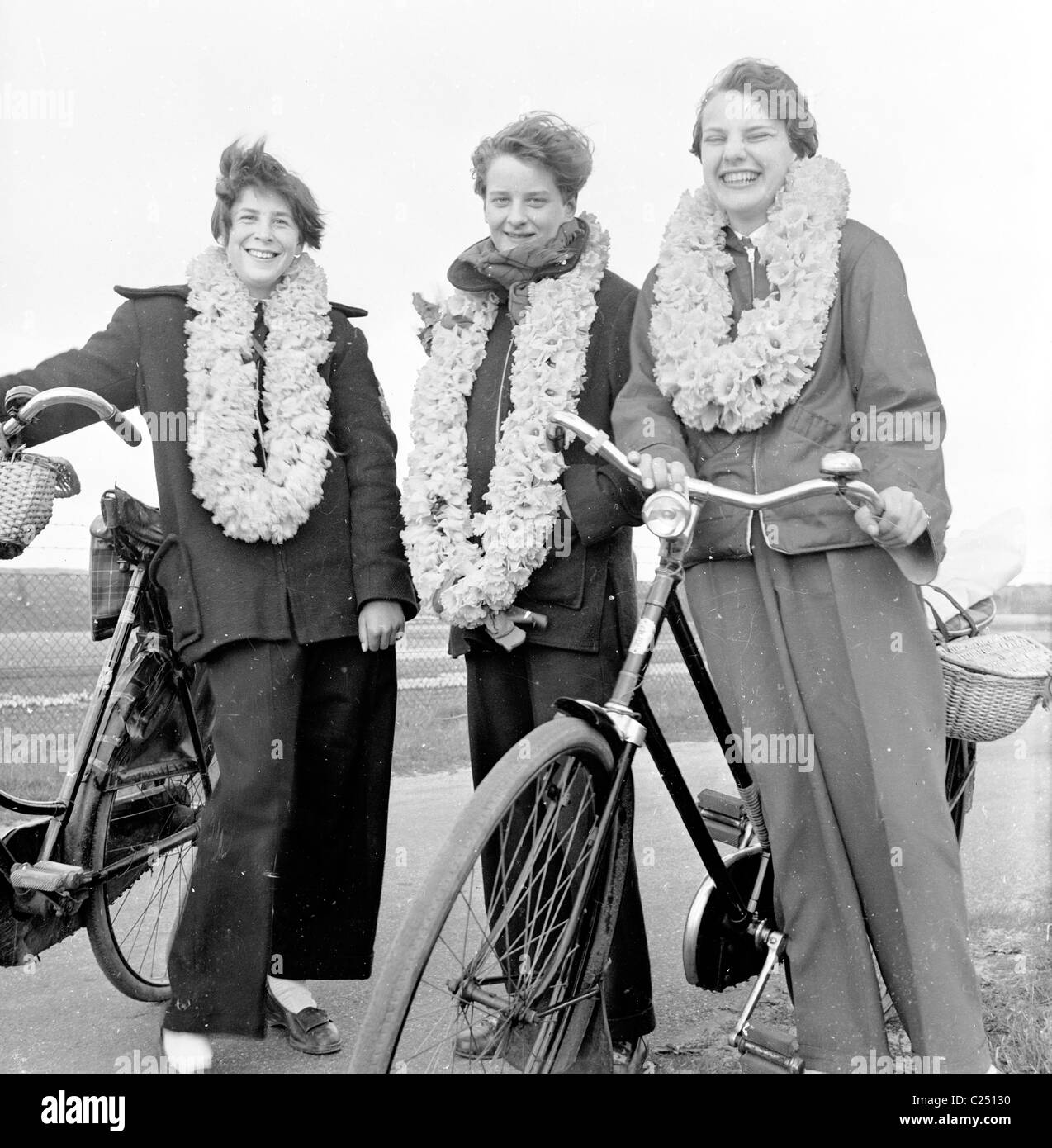 Quindi Paesi Bassi, 1950s. Tre olandese ciclisti femmina stare accanto a biciclette con fiore giunchiglie mazzi intorno ai loro colli. Foto Stock