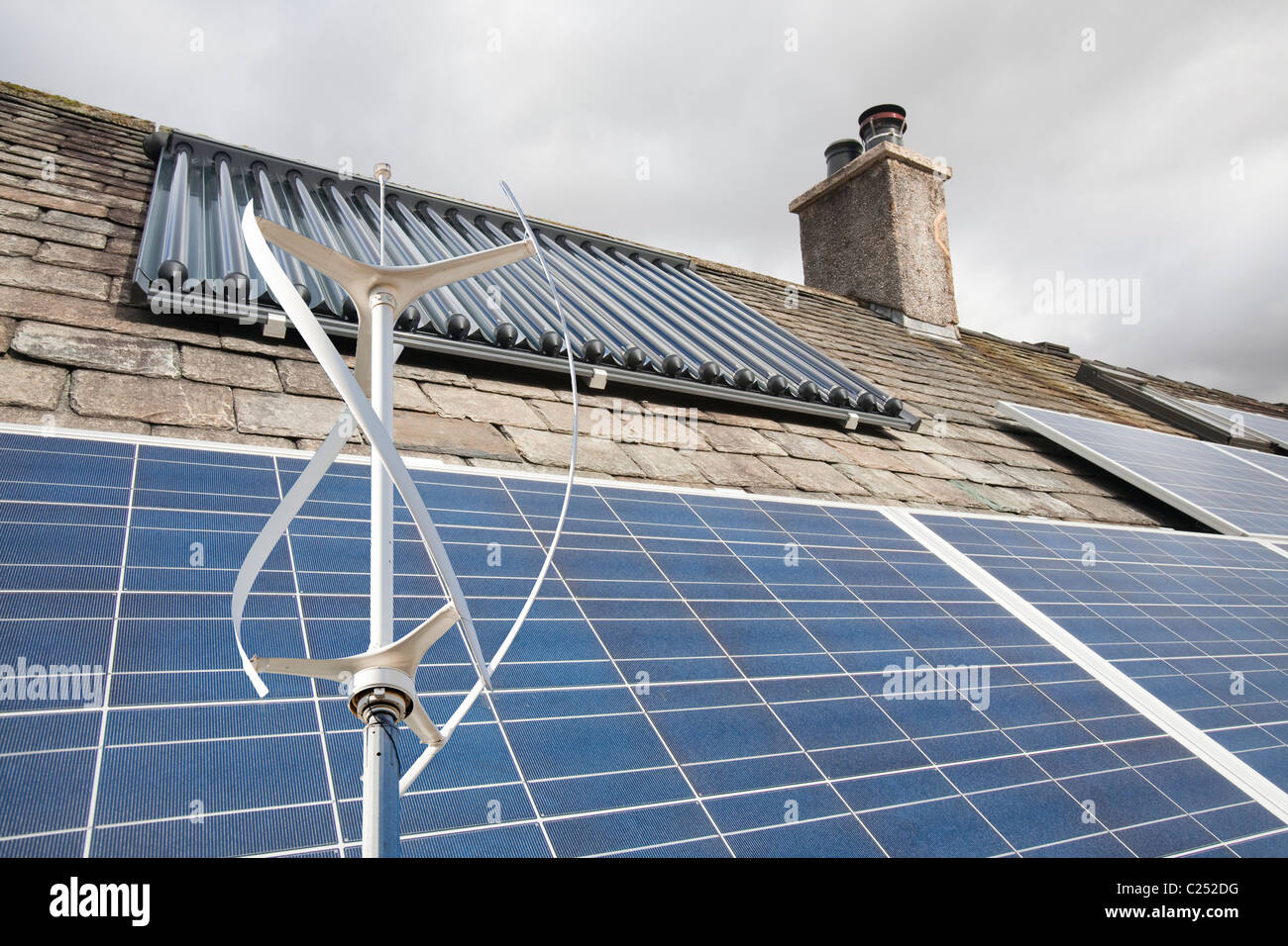 Energia solare fotovoltaica di generazione di energia elettrica e di pannelli solare di acqua calda pannelli su un tetto di casa a Ambleside, plus turbina eolica. Foto Stock