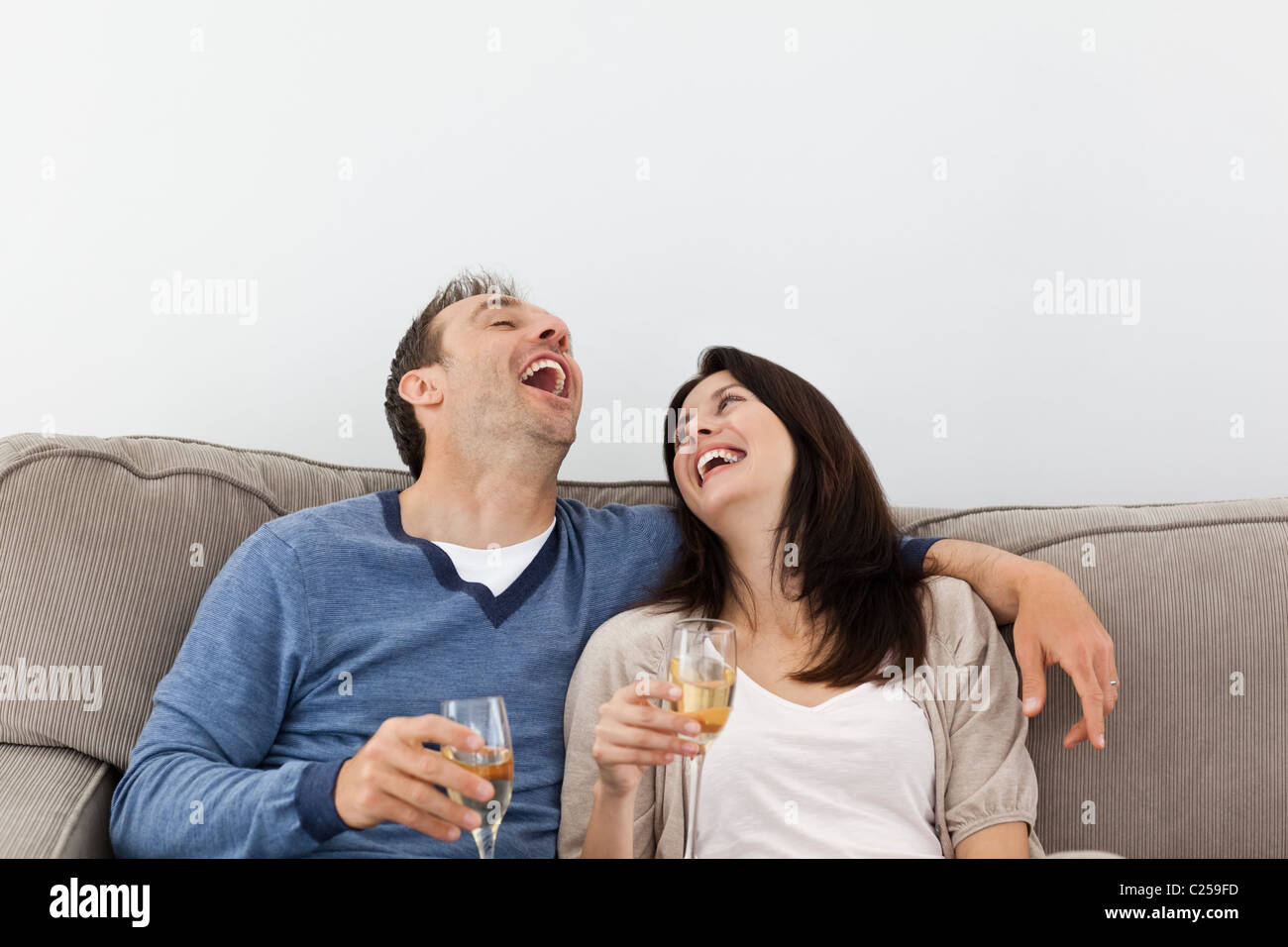 Paio di ridere mentre bevendo champagne sul divano Foto Stock