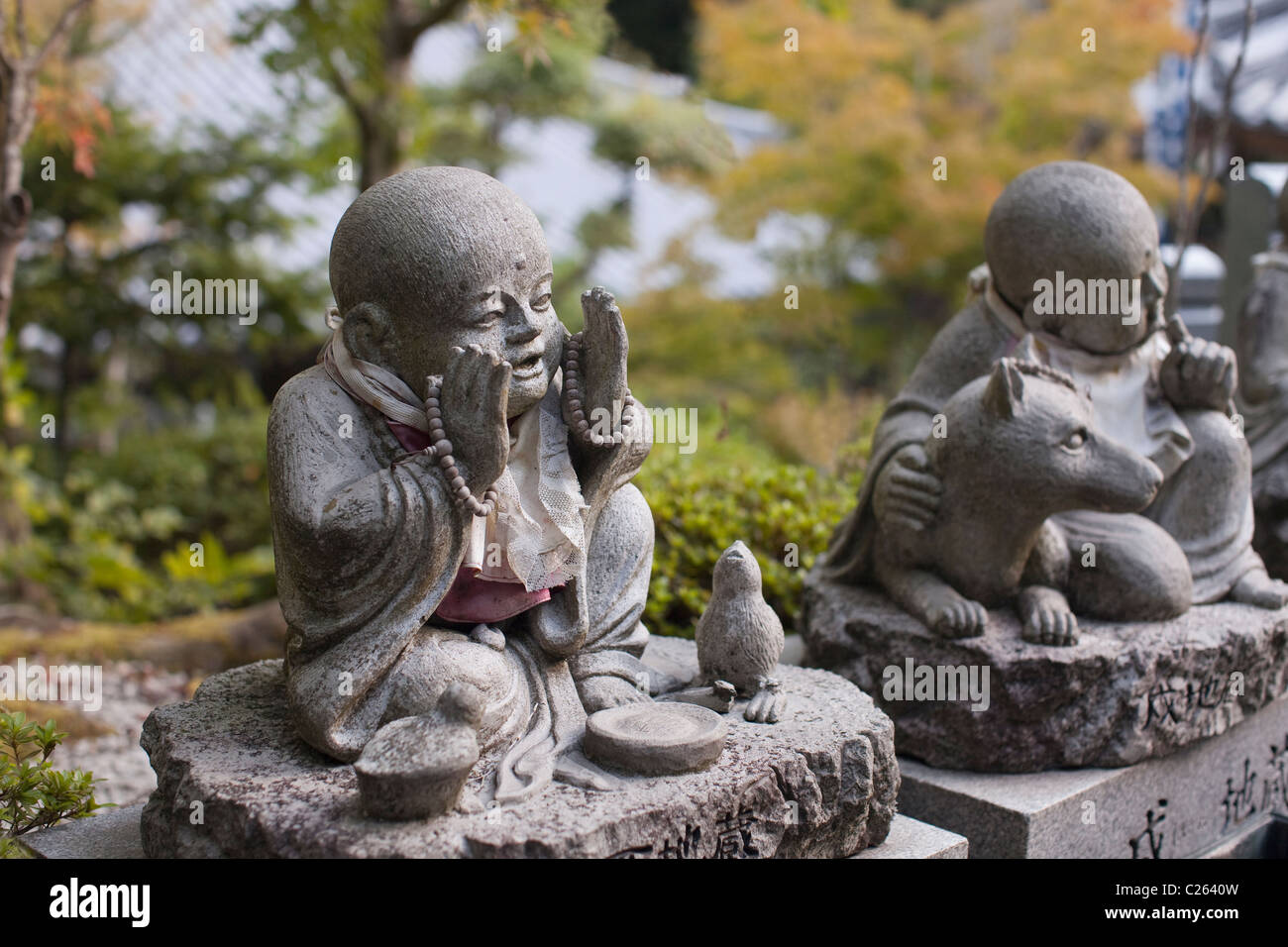 Bianco-bibbed statue con grani di preghiera, bird e cane a Daisho-nel tempio, Miyajima, Hiroshima, Giappone, Asia. Foto Stock