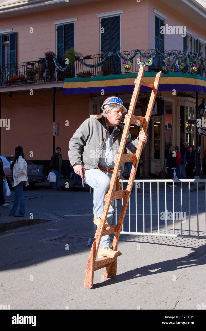 Street performance artista vestito come un lavoratore edile scalata di un free-standing scaletta in New Orleans Foto Stock
