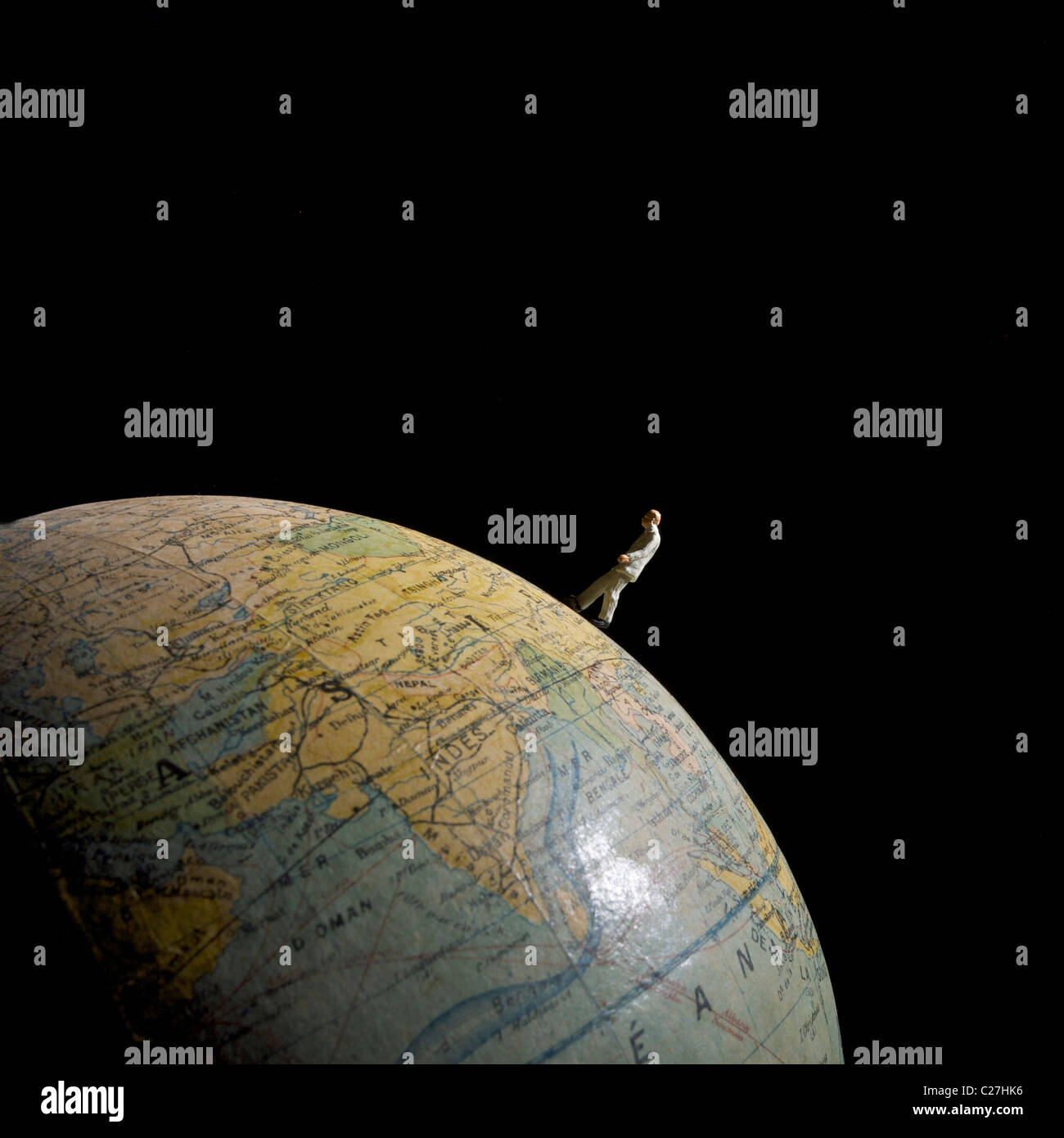 Prospettiva di una minuscola figura in piedi su un globo su uno sfondo nero in una rappresentazione creativa dell'esplorazione Foto Stock