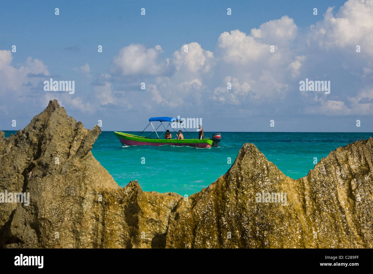 Un colorato di manovra in barca nel mare dei Caraibi con turisti e di una formazione di roccia in primo piano vicino a la Playa Tulum Messico Foto Stock