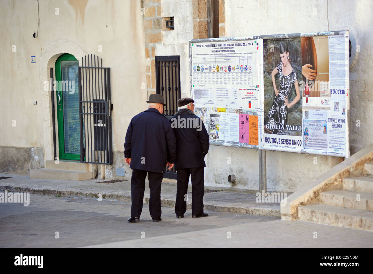 L'Italia, Cisternino, due uomo vecchio a piedi attraverso la città vecchia e guardando la pubblicità con la donna Foto Stock