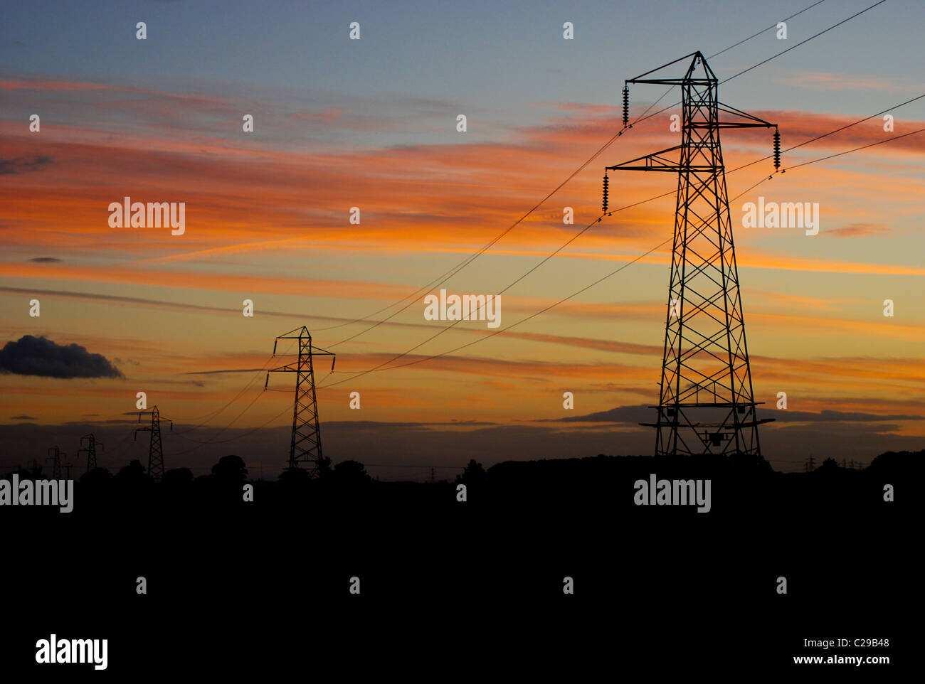Tramonto dietro una serie di linee di potenza e piloni Foto Stock