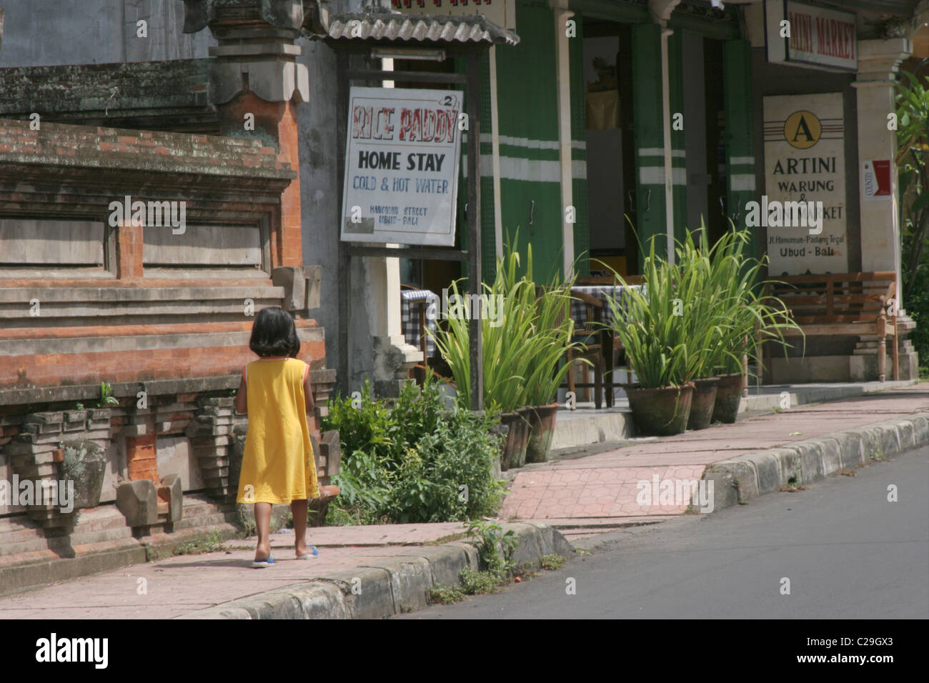 Ragazza Balinese in un abito giallo a piedi giù per una strada in Ubud, Bali. Foto Stock