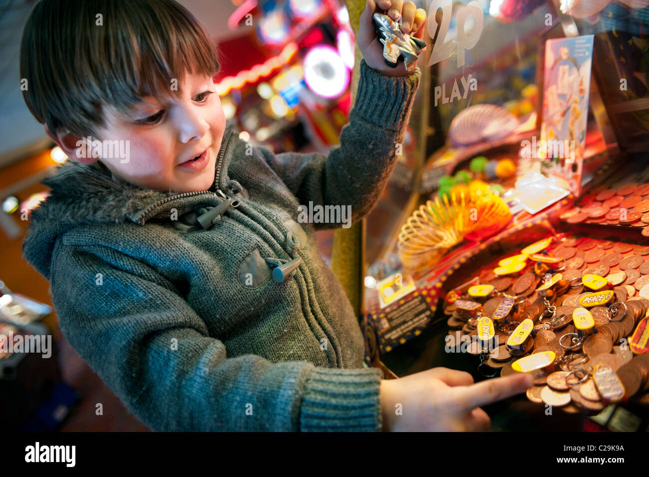 Un entusiasta piccolo ragazzo giocando le scanalature del penny un divertimento arcade Foto Stock