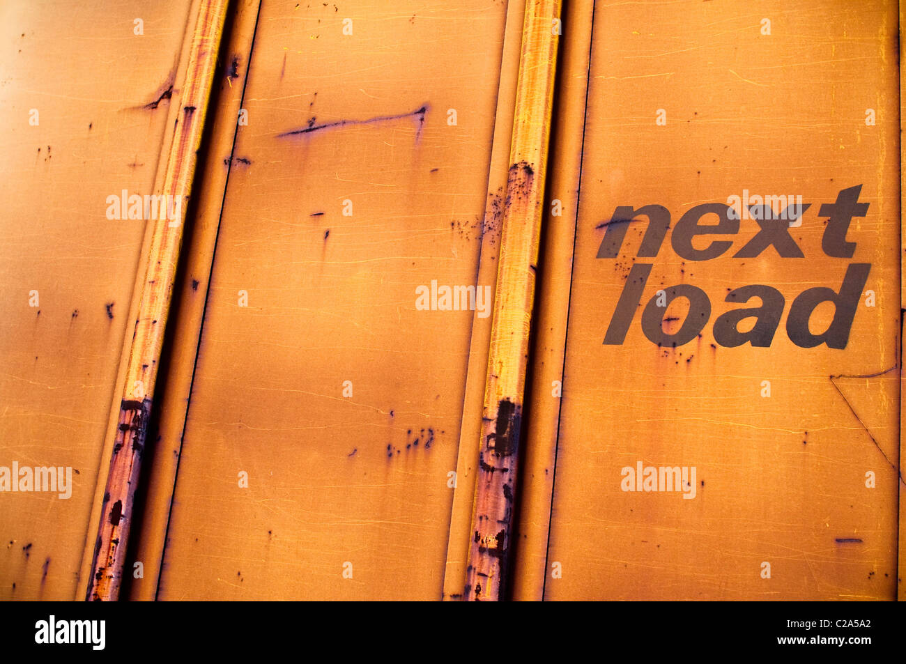 La formazione di ruggine lato di un vecchio treno merci auto, con le parole "carico successivo' con lettere in neretto. La vettura presenta ruggine graffi. Foto Stock