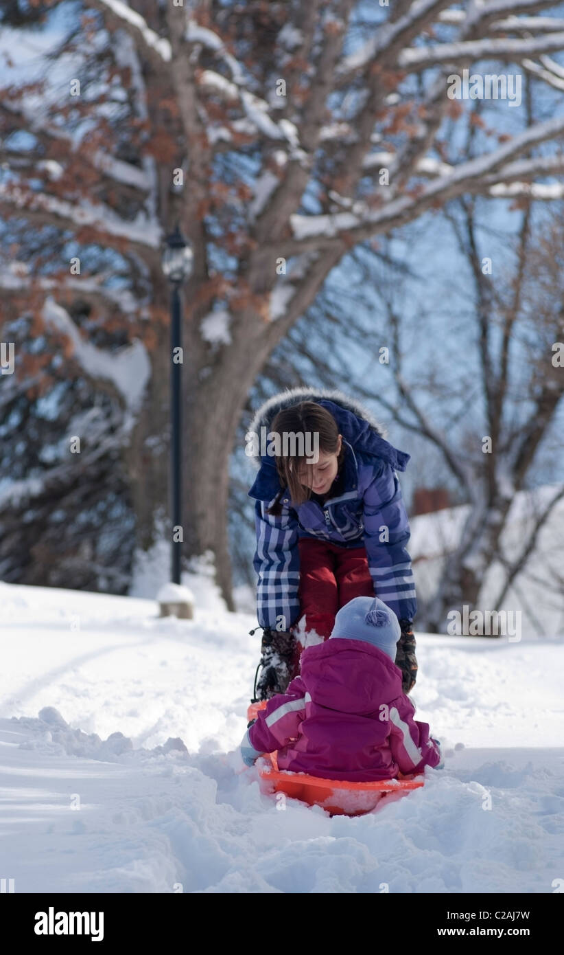 I vecchi Ragazza tira i suoi tre-anno-vecchia sorella in una slitta in un giorno di neve a fine febbraio in Pennsylvania. Foto Stock