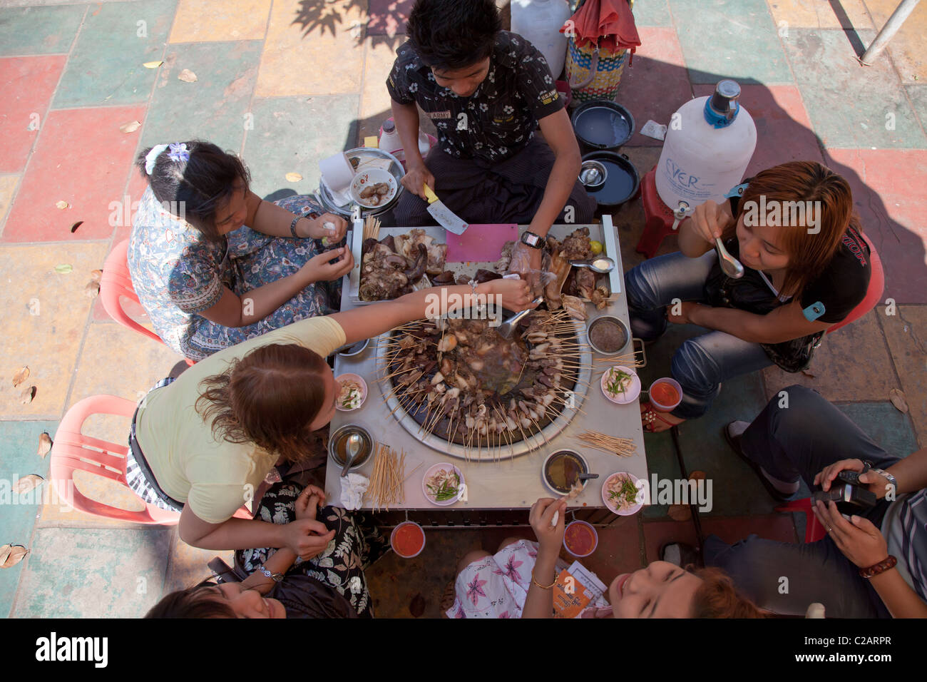 Un gruppo di giovani stanno mangiando fatta in casa il cibo nel mercato di strada ristorante. Rangoon, la Birmania. Foto Stock