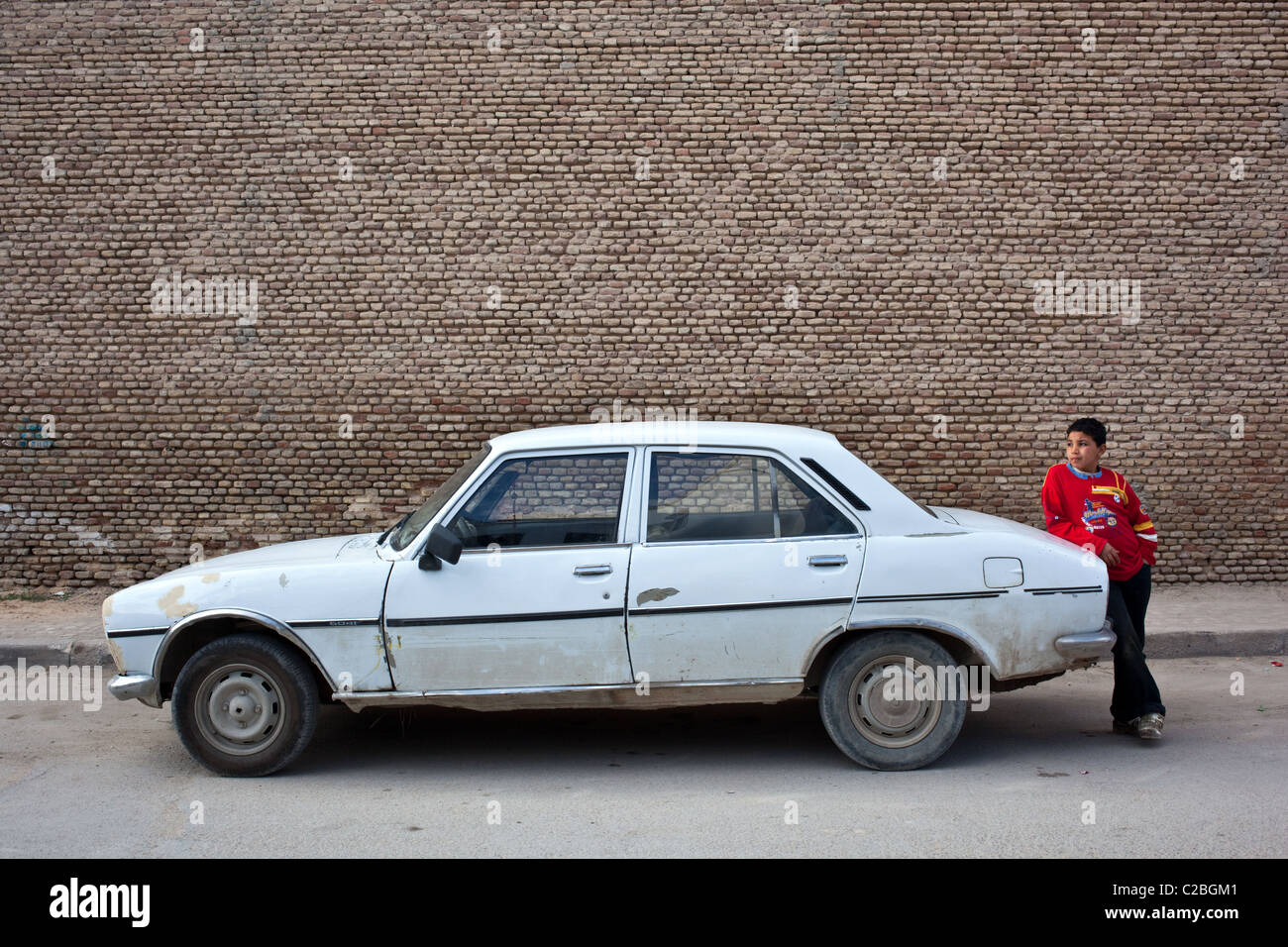 Un giovane ragazzo si erge un vecchio di Peugeot 504 auto nella città vecchia di UNESCO di cui Kairouan city, Tunisia. Foto Stock