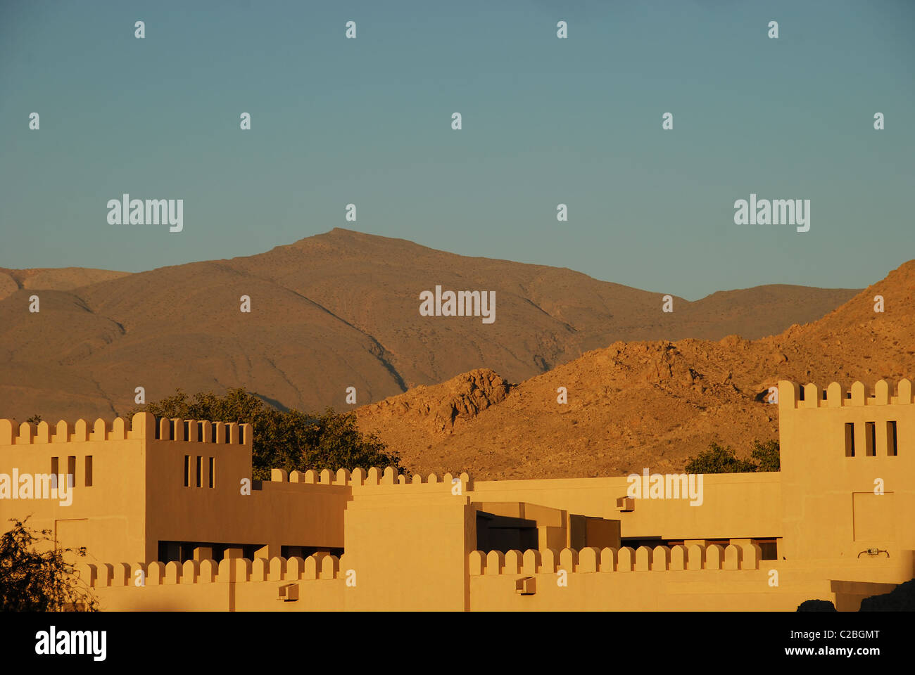 Oman, Nizwa, la vista di vecchi edifici storici nella parte anteriore del mountain contro il cielo blu chiaro Foto Stock