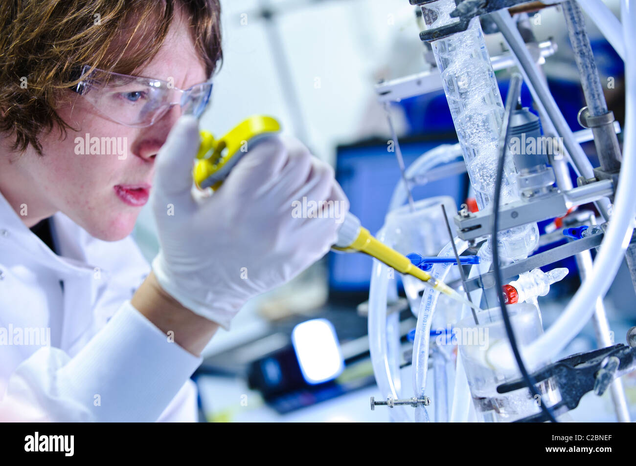 Giovane maschio scienziato che indossa gli occhiali e white lab umettare il pipettaggio in apparecchio scientifico nel laboratorio di scienze Foto Stock