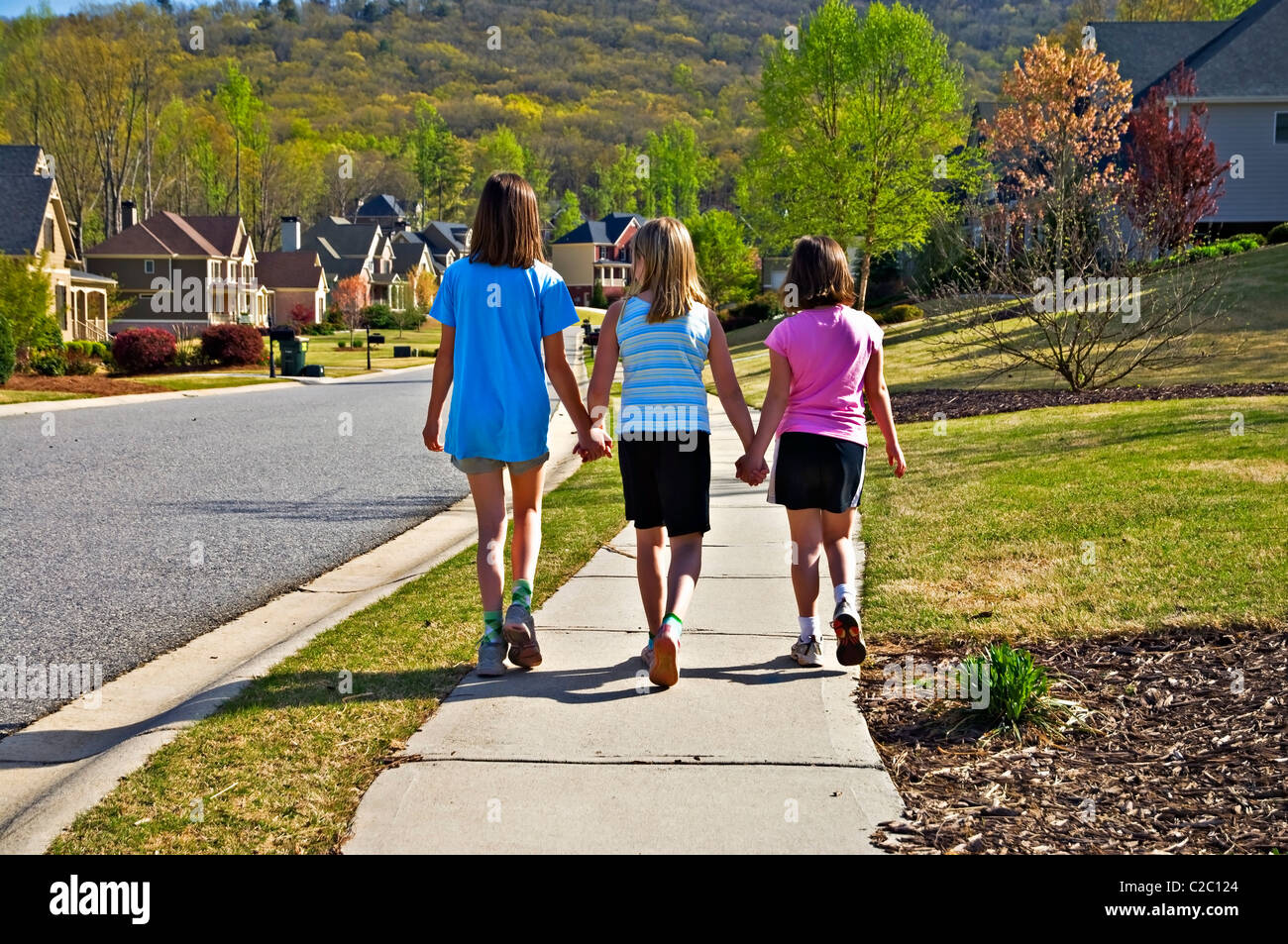 Tre giovani ragazze camminare insieme su un marciapiede in un quartiere tenendo le mani. Foto Stock