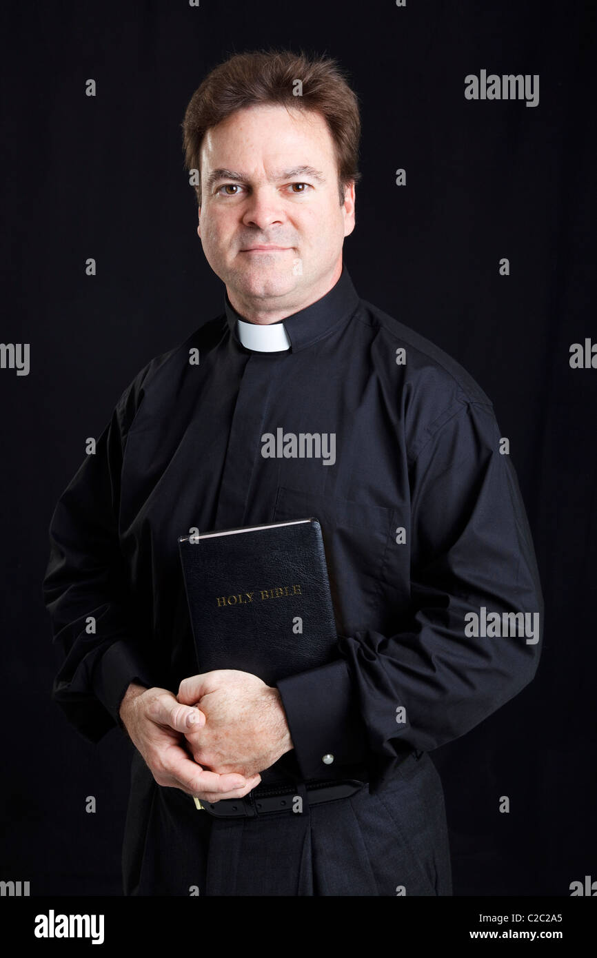 Ritratto di un prete cattolico tenendo la bibbia. Sfondo nero. Foto Stock