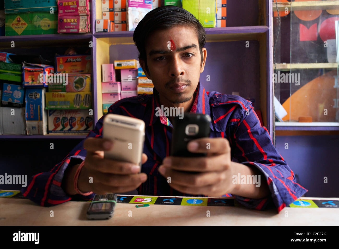 Un negoziante nel suo telefono mobile store tops-fino a un telefono cellulare, Varanasi (India). Foto Stock