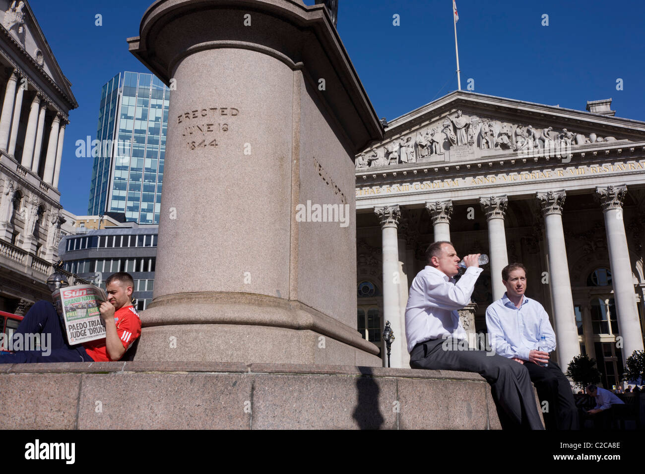 Un quotidiano Sun reader e di imprenditori al di sotto di una statua a Royal Exchange dietro. Foto Stock