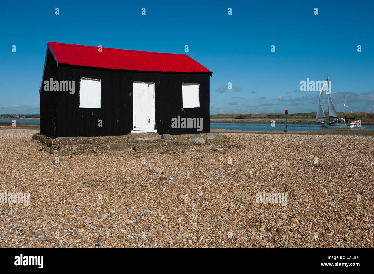 Bianche vele yacht passato NORTONS capanna sulla spiaggia di ciottoli della segala Harbor East Sussex con un parco eolico a distanza Foto Stock