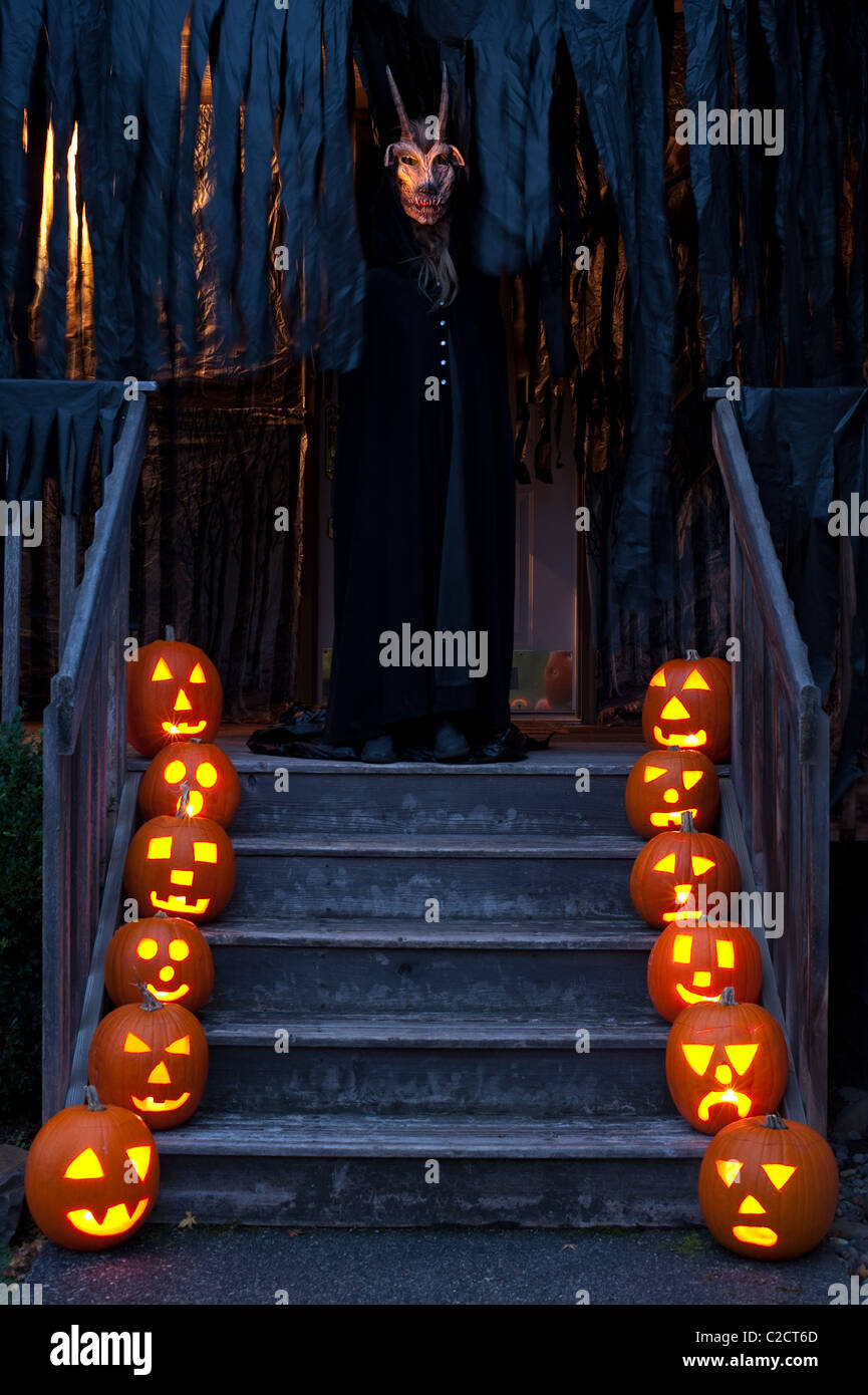 Scary accesa scolpite zucche di twilight su scale con demone con corna sulla veranda Haunted House su Halloween Foto Stock