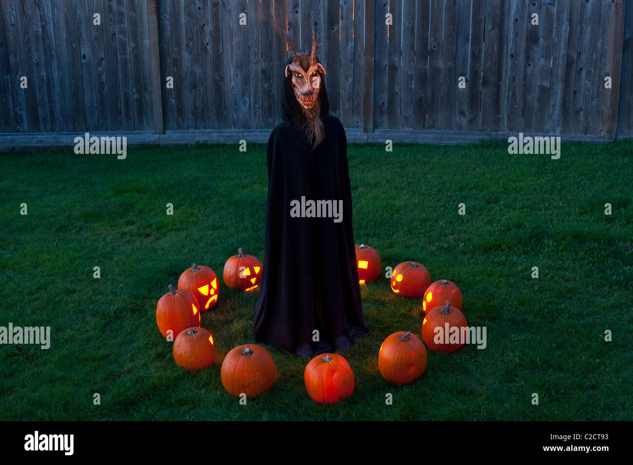 Scary lit zucche intagliate al crepuscolo demone con corna candela in un cerchio seance in un cortile di Halloween Foto Stock