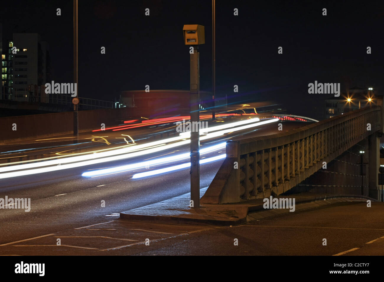 Sentieri di luce dei veicoli che passano a un autovelox di notte su Aspen modo vicino a Canary Wharf a Londra, Inghilterra Foto Stock