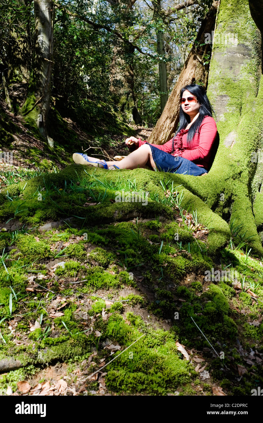 Giovane donna relax su un muschio coperto banca in un luminoso bosco Foto Stock