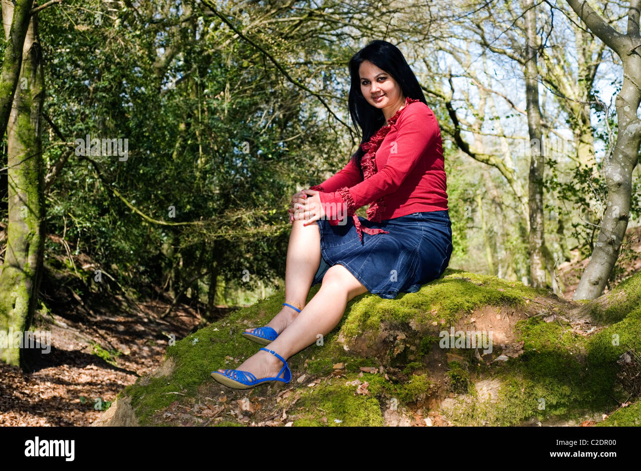 Giovane donna relax su un muschio coperto banca in un luminoso bosco Foto Stock