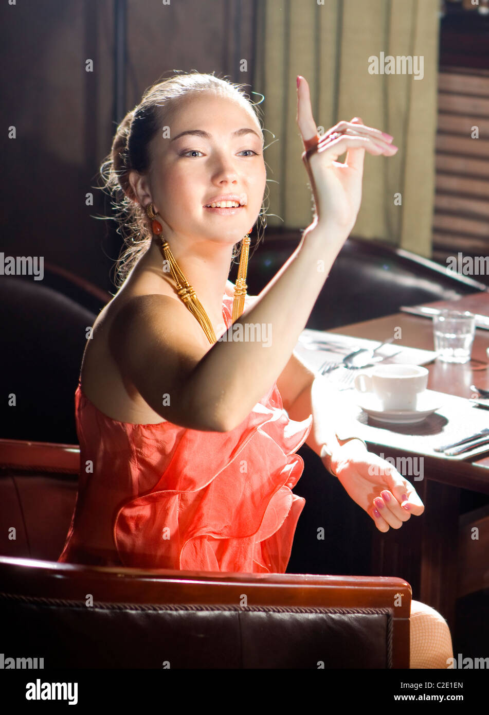 La donna si siede a tavola e fa un segno al cameriere al ristorante Foto Stock