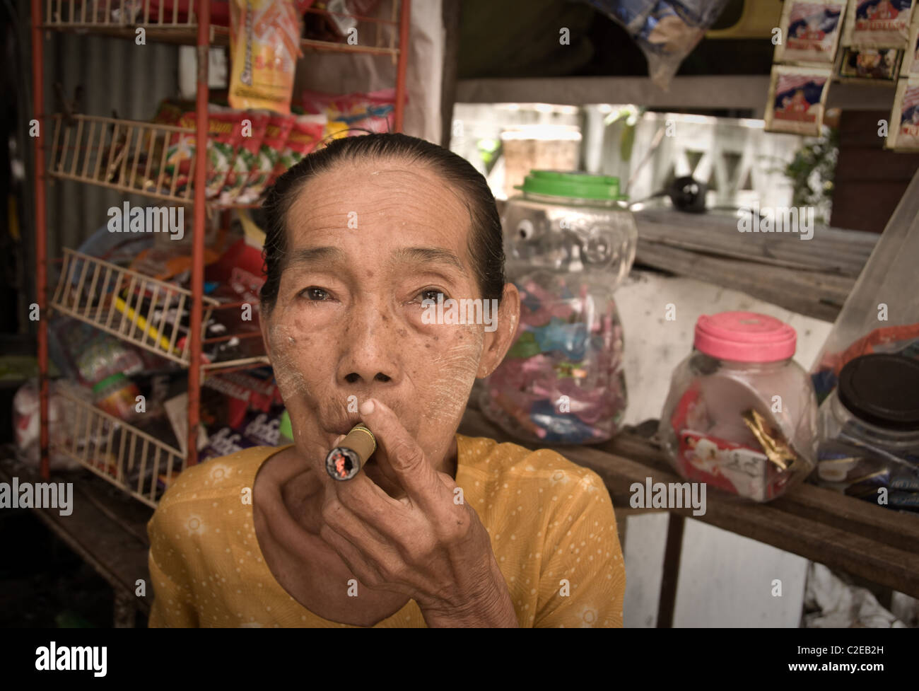 Pyay, birmania, myanmar - Luglio 2010: il proprietario di un negozio di fumare la tradizionale sovradimensionato sigaro birmano Foto Stock