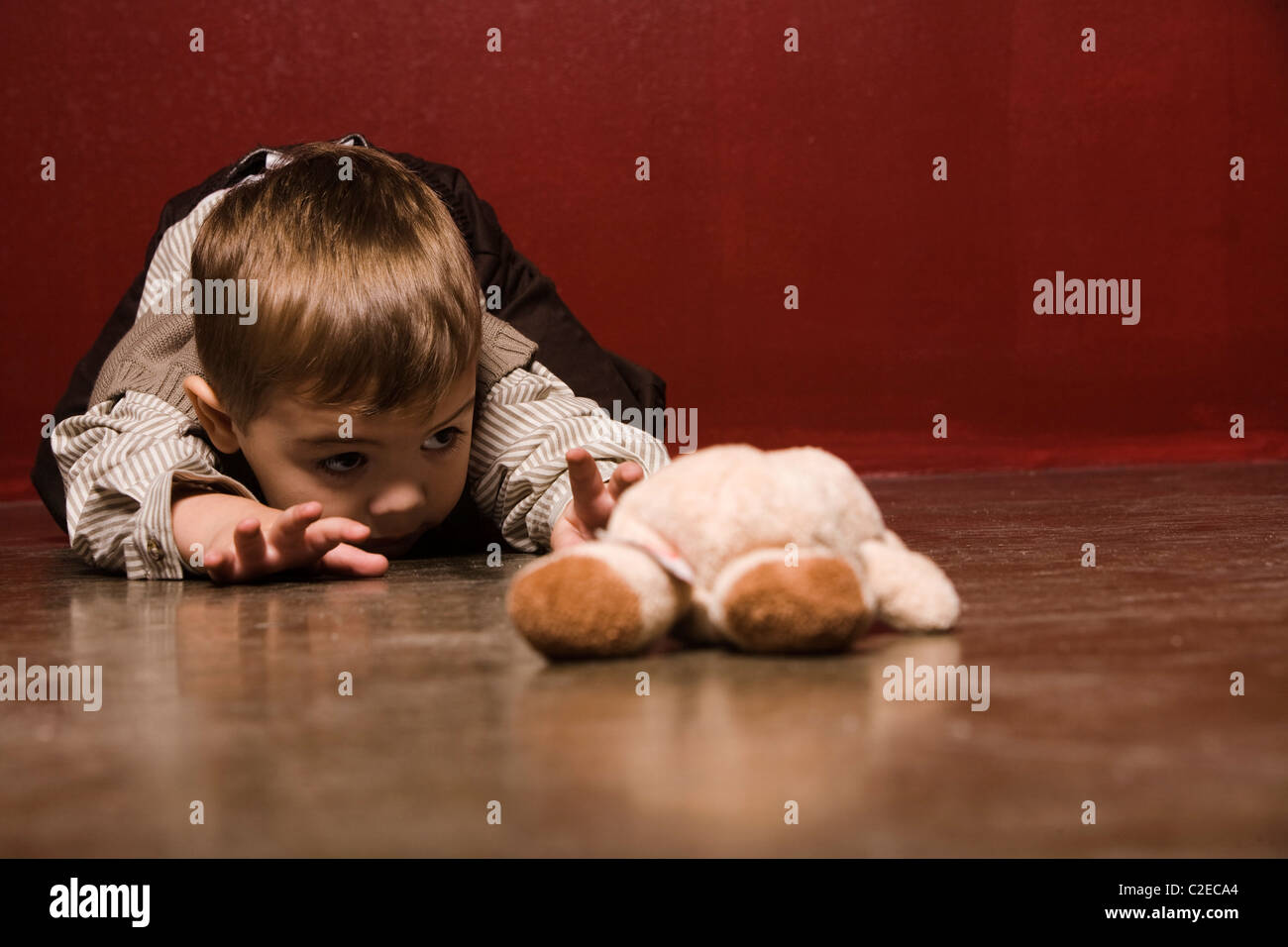 Il Toddler strisciare sul pavimento per raggiungere Orsacchiotto Foto Stock