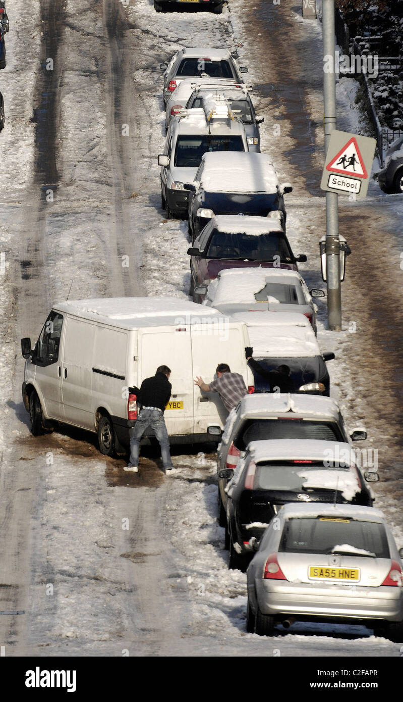 Due uomini spingere un furgone su una strada in salita a Glasgow in Scozia che è ricoperto di ghiaccio e neve, rendendo la guida e camminare difficile. Foto Stock