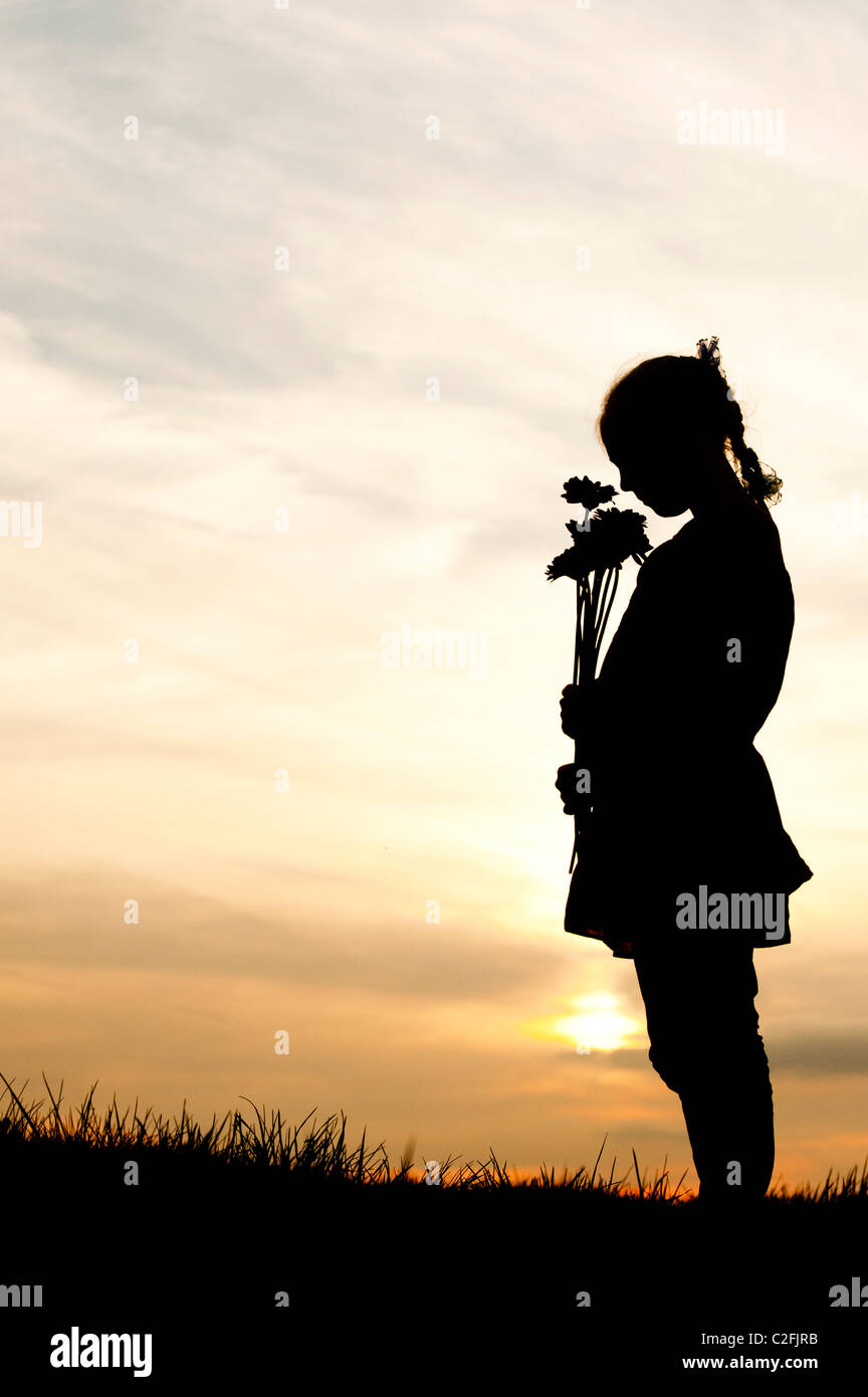 Solitaria ragazza giovane azienda permanente di fiori contro un tramonto. Silhouette Foto Stock