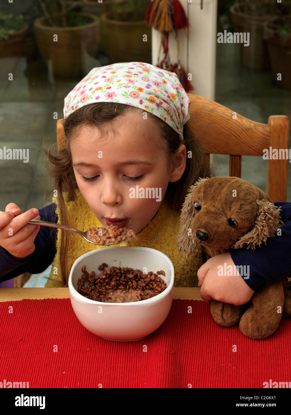 Ragazza giovane mangiare cereali a colazione tenendo un cane Soft Inghilterra Foto Stock
