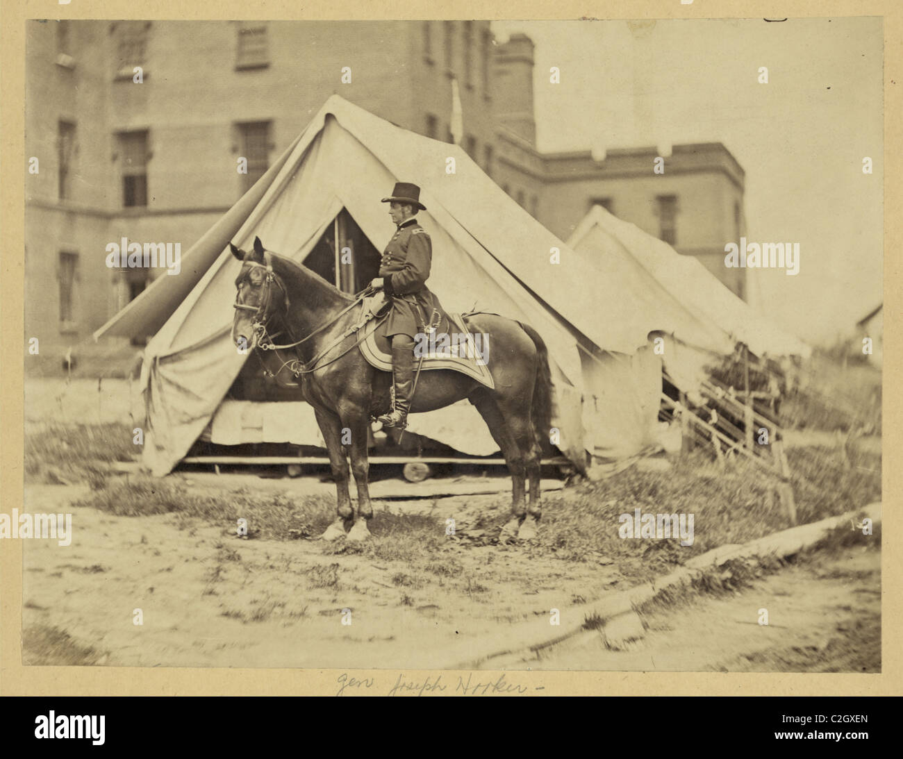 General Maggiore Joseph Hooker di intera lunghezza verticale, seduto sul cavallo, rivolto verso sinistra, indossando uniforme militare, due tende e il grande edificio in background Foto Stock