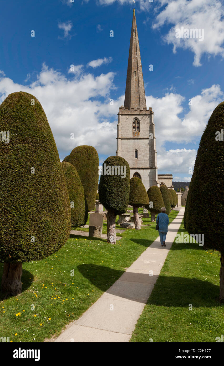 PAINSWICK chiesa Chiesa e cortile con alberi di tasso con la donna camminando sul percorso IN PAINSWICK,i Cotswolds, GLOUCESTERSHIRE, INGHILTERRA Foto Stock