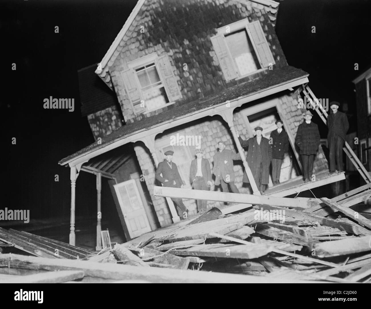 Gli uomini di stand sul portico di un mare luminoso Cottage strappato dalla sua fondazione ed inclinato di un angolo di 45 gradi. Foto Stock