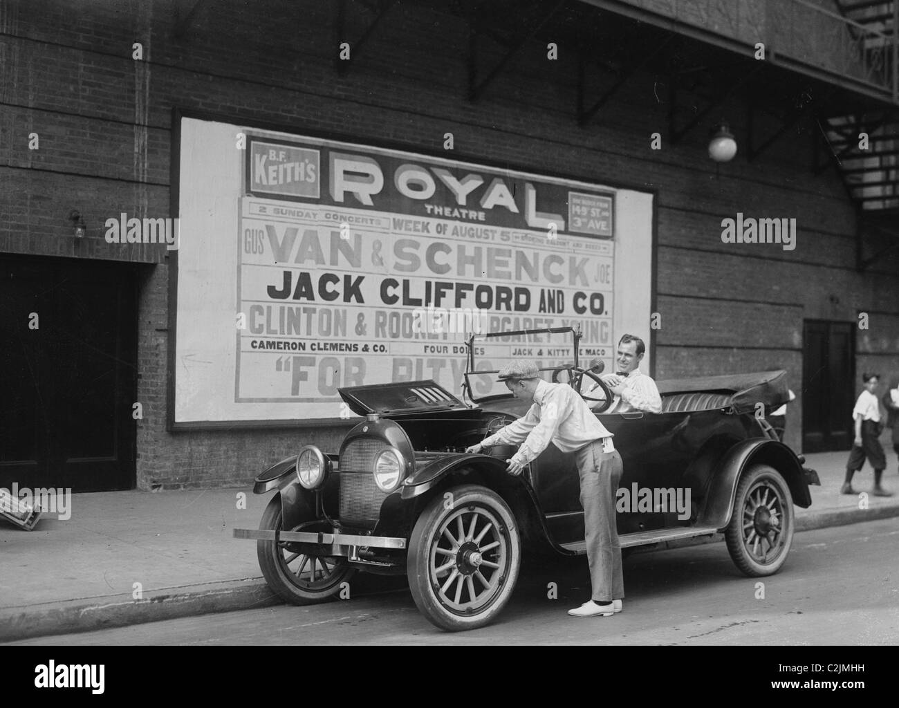 Due interpreti lavorano sui loro auto, uno nel driver' sedile e l'altra guarda sotto il cofano; Van & Schenk Foto Stock