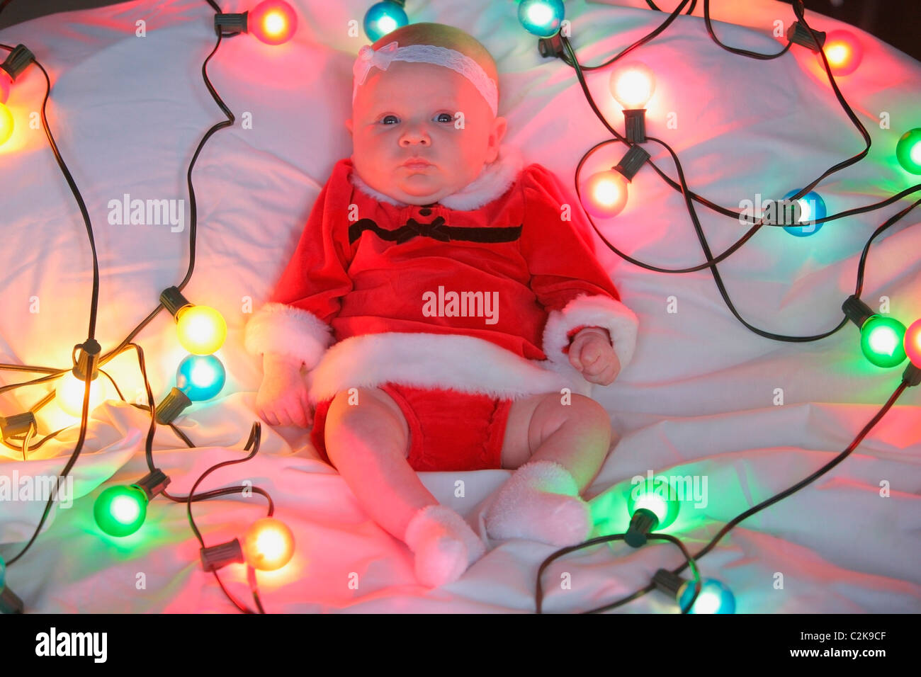 Un neonato Ragazza in un abito di Natale circondato da una stringa di luci Foto Stock