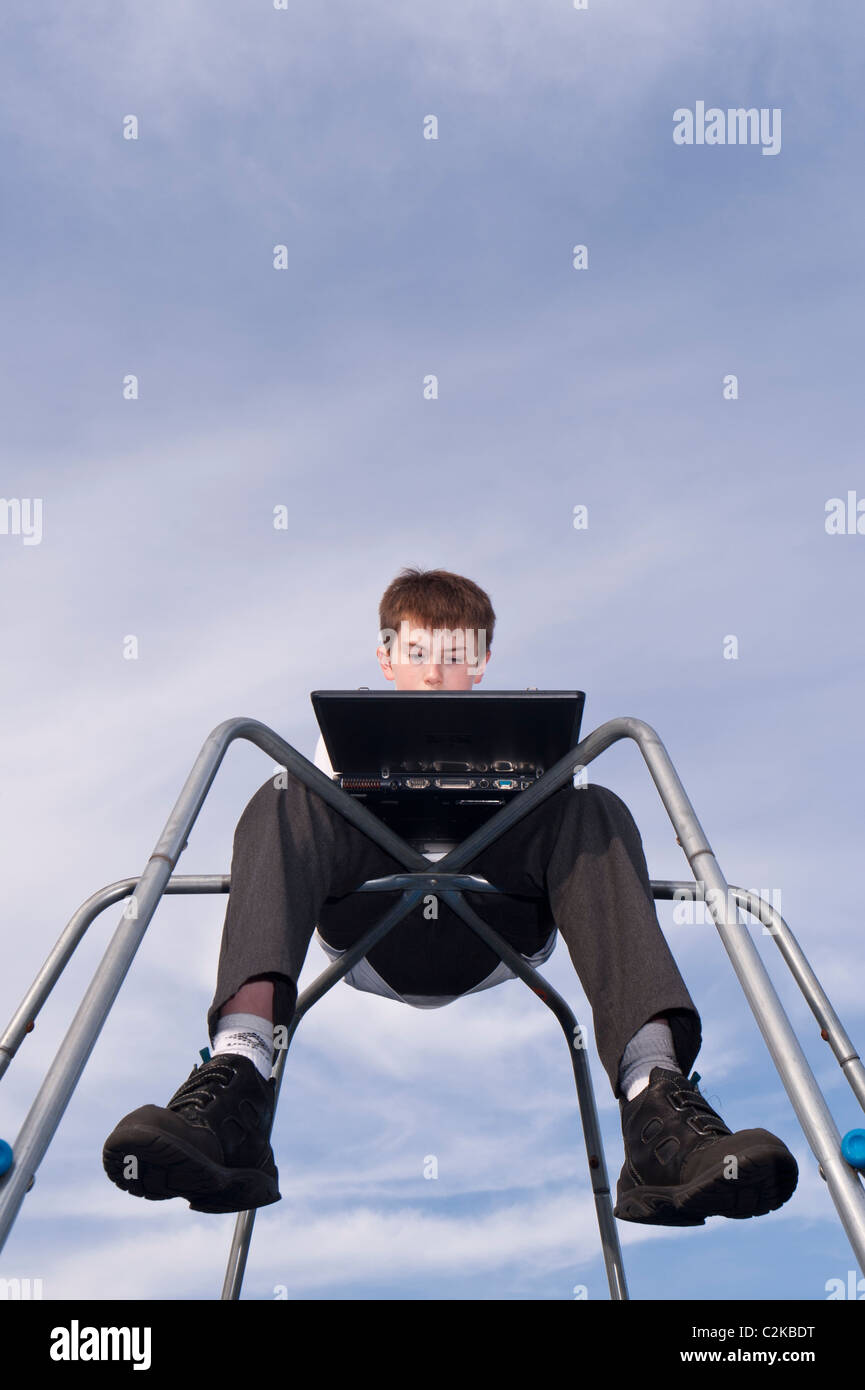 Un modello rilasciato la foto di un ragazzo di undici anni usando il suo computer portatile all'aperto su un telaio di arrampicata nel Regno Unito Foto Stock