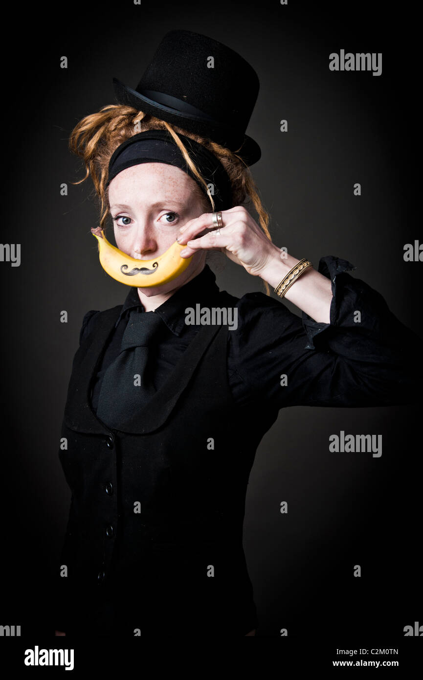 Giovani alt punky funky donna tenendo una banana con un baffi disegnato che oltre la sua bocca Foto Stock