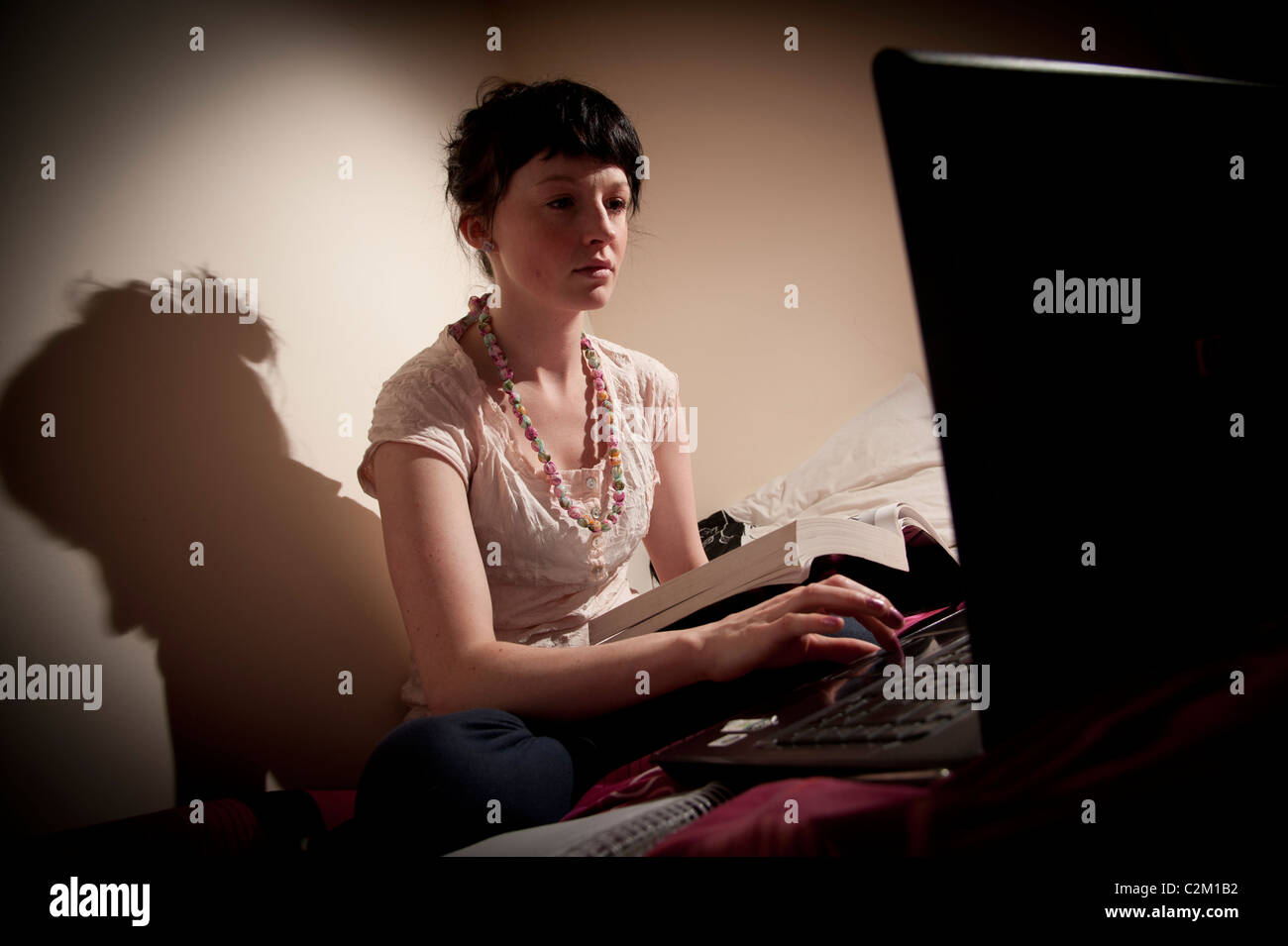 Una giovane donna femmina ragazza UK università studenti che lavorano sul suo computer portatile nella sua camera da letto a casa Foto Stock